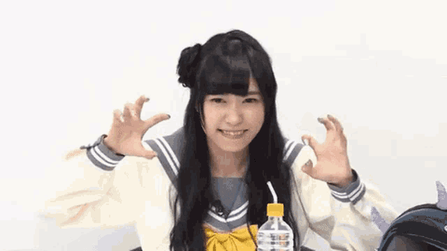 a girl in a school uniform is sitting at a table with a bottle of water in her hand .