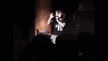a man is singing into a microphone while wearing a black shirt that says ' we are ' on it .