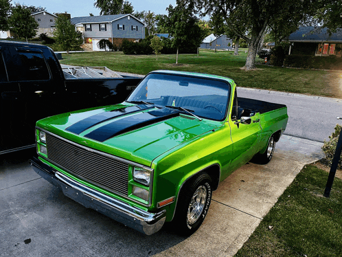 a green truck with a black stripe on the hood is parked on a sidewalk