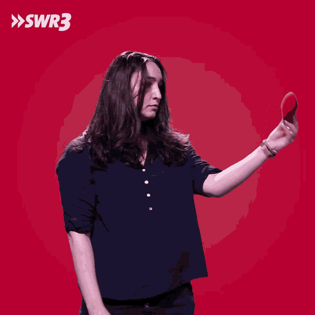 a woman in a blue shirt is pointing at a red object in front of a red background with the letters swr3 on it