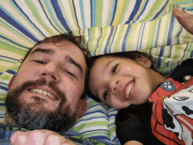 a man and child are laying under a striped blanket and smiling
