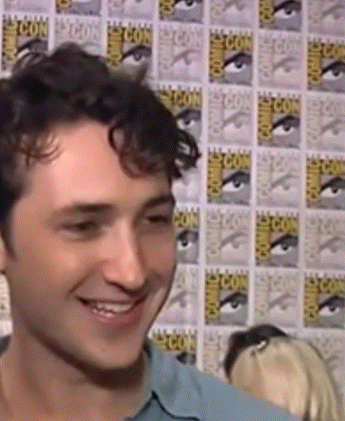 a man is smiling in front of a wall that says comic con on it
