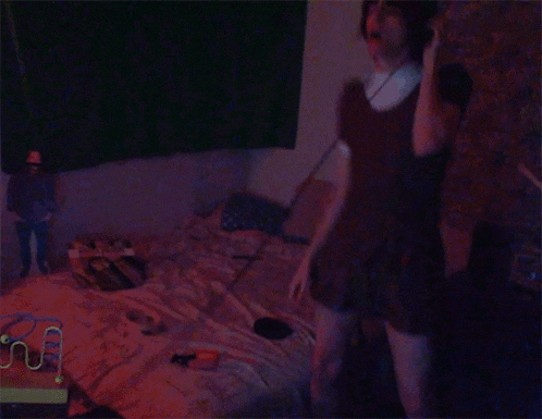 a person standing in a dark room with a doll on the bed