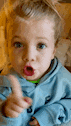 a young boy is pointing at the camera with his mouth open .