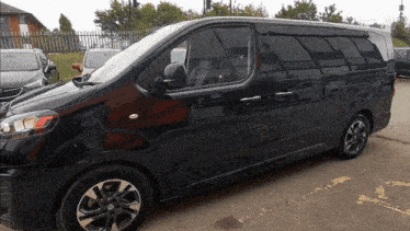a black van is parked in a parking lot with a fence in the background