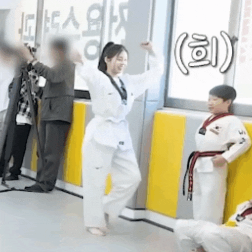 a woman in a taekwondo uniform is dancing in front of a group of people in a room .