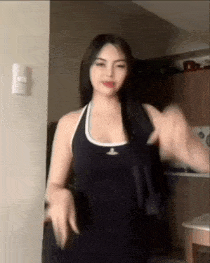 a woman is standing in a kitchen wearing a black tank top and dancing .