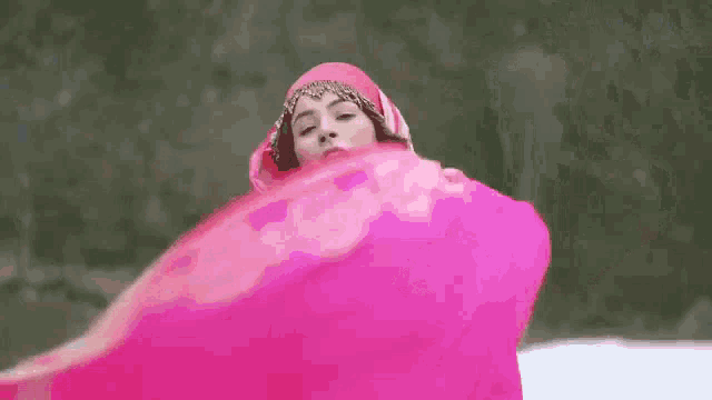 a woman in a pink dress is dancing in the snow with a pink scarf .