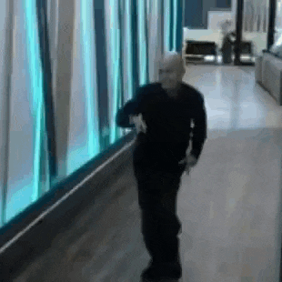 a man in a black shirt is walking down a hallway in front of a blue wall .