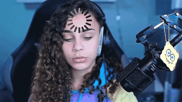 a girl sitting in front of a microphone with a spongebob keychain hanging from it