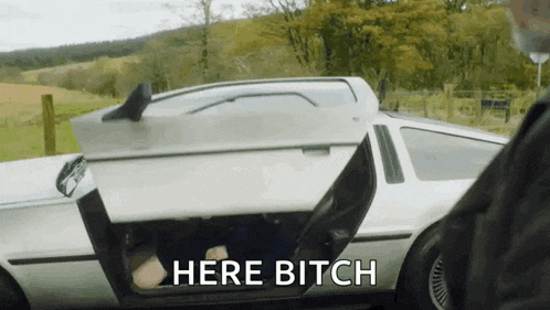 a man is driving a car with the door open and the words `` here bitch '' written on the bottom .