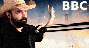 a man wearing a cowboy hat stands in front of a bbc advertisement