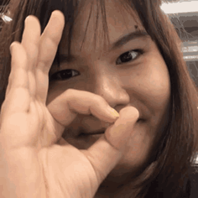 a woman is making a heart shape with her fingers and smiling .