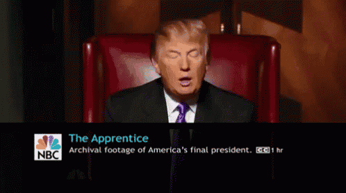 a man in a suit and tie is sitting in front of a screen that says the apprentice on it
