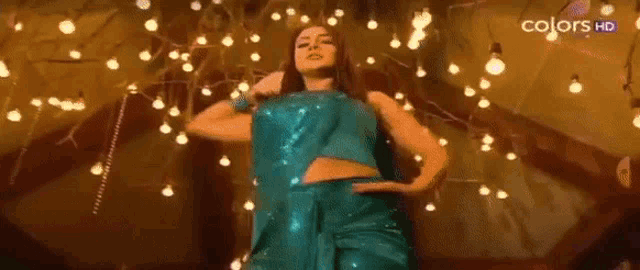 a woman in a blue dress is dancing in a room with lights hanging from the ceiling .