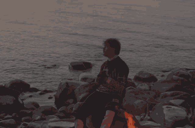a person sitting on a rock near a fire with a shirt that says ' i love you '