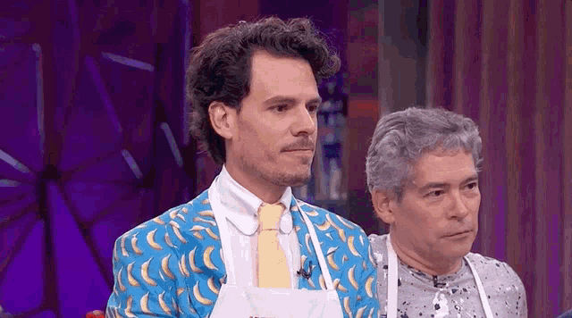 two men are standing next to each other on a stage . one of the men is wearing a banana suit .