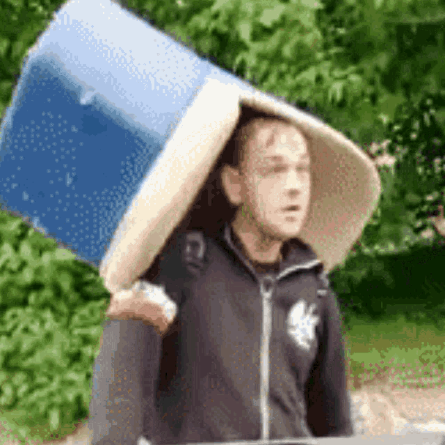 a man is carrying a large blue bucket on his head