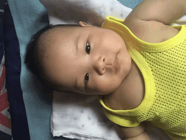 a baby wearing a yellow tank top is laying on a blanket