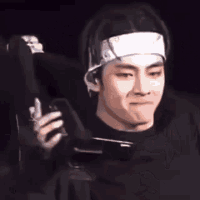a man with a bandage on his head is holding a cell phone in his hand .