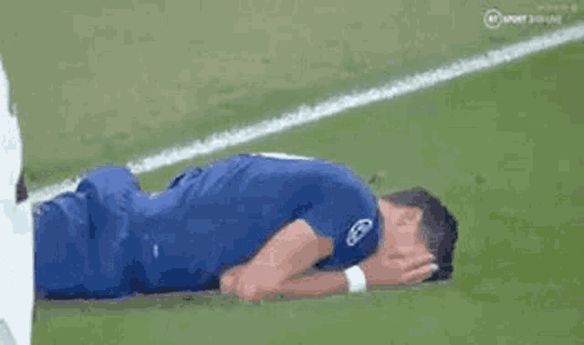 a soccer player is laying on the ground with his head in his hands on the field .
