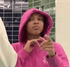 a girl wearing a pink hoodie is making a heart with her hands .