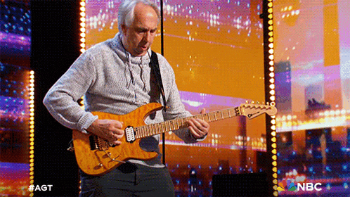 a man playing a guitar on a stage with a nbc logo in the background