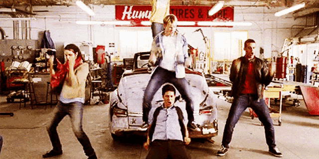 a group of men are dancing in front of a hum tires and tires sign
