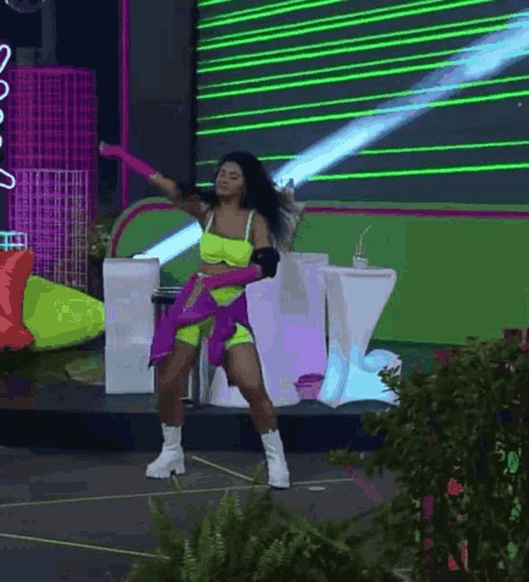 a woman in a neon outfit is dancing on a stage in front of a green screen .