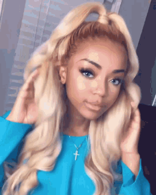 a woman with blonde hair is wearing a blue sweater and a necklace with a cross .