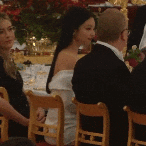 a woman in a white dress is sitting in a wooden chair next to a man in a black suit .