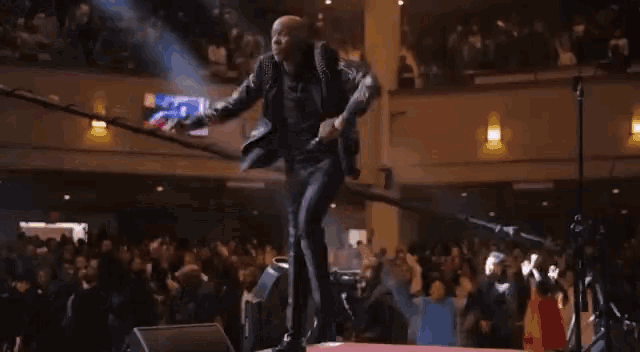 a man in a leather jacket is dancing on stage in front of a crowd