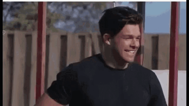 a man in a black shirt is smiling while standing next to a fence .