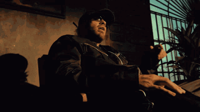 a man wearing a hat and sunglasses is sitting in a dark room