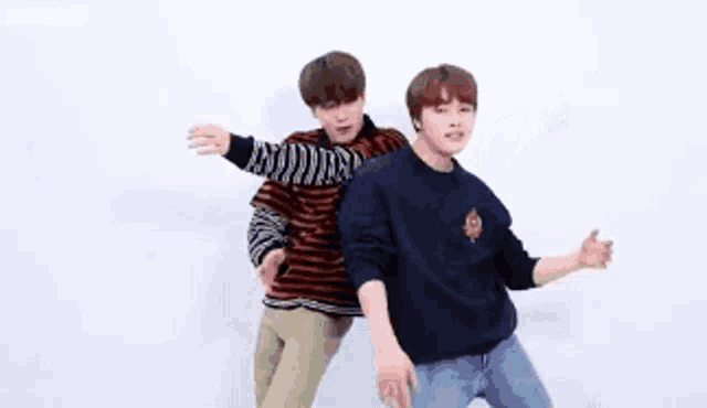 two young men are standing next to each other and dancing in front of a white wall .