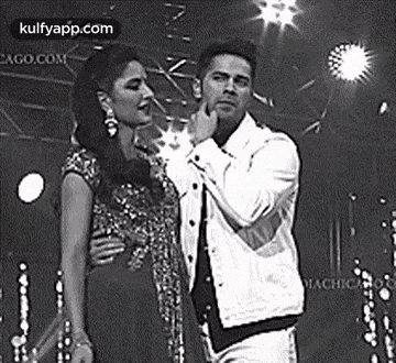 a man and a woman are standing next to each other on a stage . the man is touching the woman 's face .