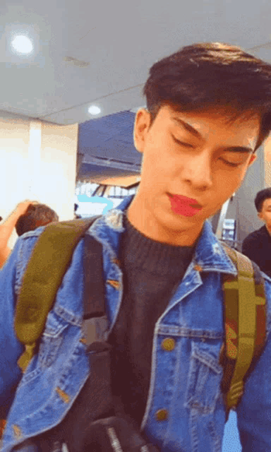a young man wearing a denim jacket and a backpack looks at the camera