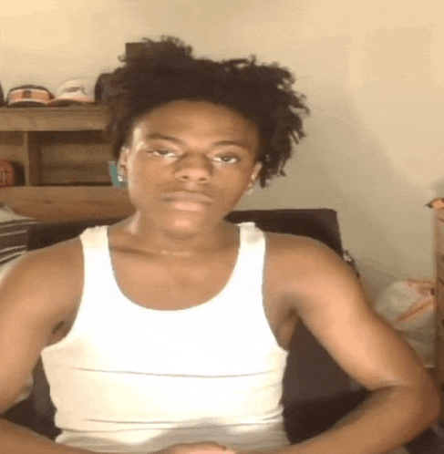 a young man wearing a white tank top is sitting in a chair