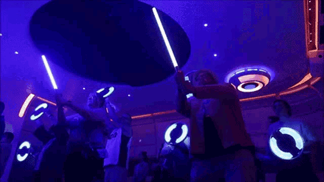 a group of people holding glow in the dark lightsabers in a room