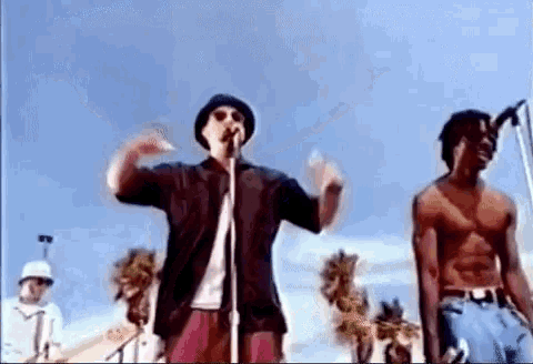 a man is singing into a microphone while a shirtless man stands next to him .