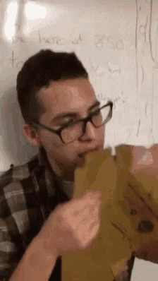 a man wearing glasses is eating a piece of paper in front of a whiteboard .