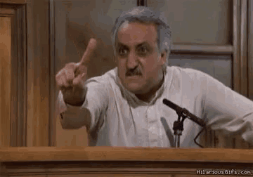 a man is giving a speech in front of a microphone in a courtroom and pointing his finger .
