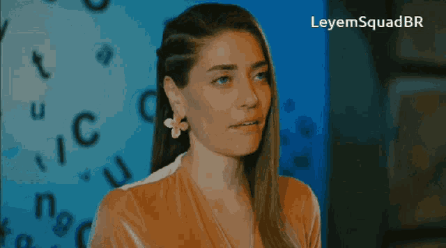 a woman wearing a flower earring stands in front of a blue wall with letters flying around her