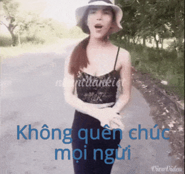a woman wearing a hat stands on a road with the words không quên chức mọi người written in blue