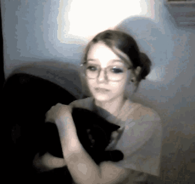 a girl wearing glasses holds a black cat in her arms
