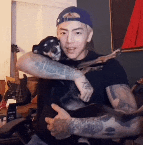 a man with a tattoo on his arm is holding a small black dog