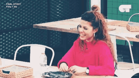a woman in a pink sweater is sitting at a table with a plate of food ..