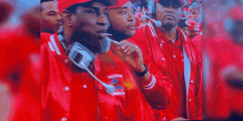 a person wearing a red jacket and a watch is standing in front of a crowd .
