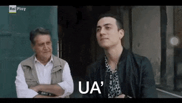two men are sitting next to each other on a sidewalk and one of them is talking to the other .