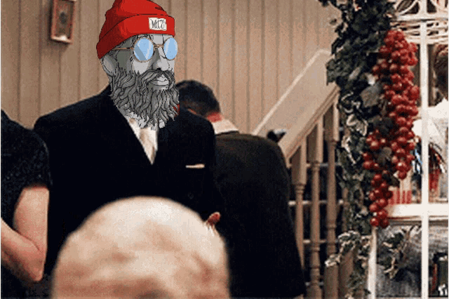 a man with a beard wearing a red beanie and sunglasses has a sticker on his hat that says n77